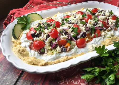 Mediterranean Layer Dip with bright cherry tomatos and in a beautiful white serving dish
