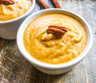 bright yellow creamy fall harvest soup in a white bowl garnished with a fresh southern pecan