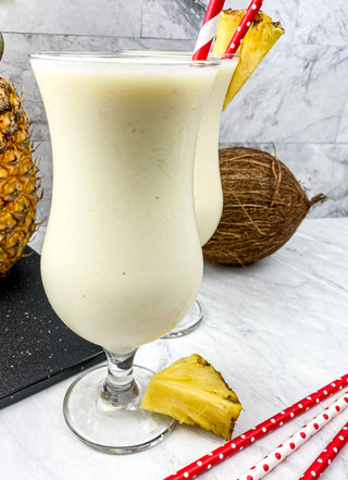 Fresh and delicious frozen pina colada in a hurricane glass with a pineapple and cocoanut in the back