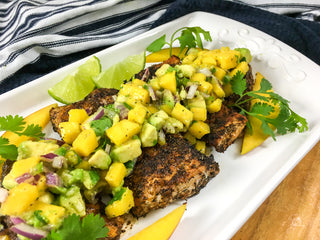 Spicy Cajun Snapper with Mango-Avocado Salsa recipe  image with bright yellow mango diced a top perfectly blackened canjun snapper on a white plate and ready to eat